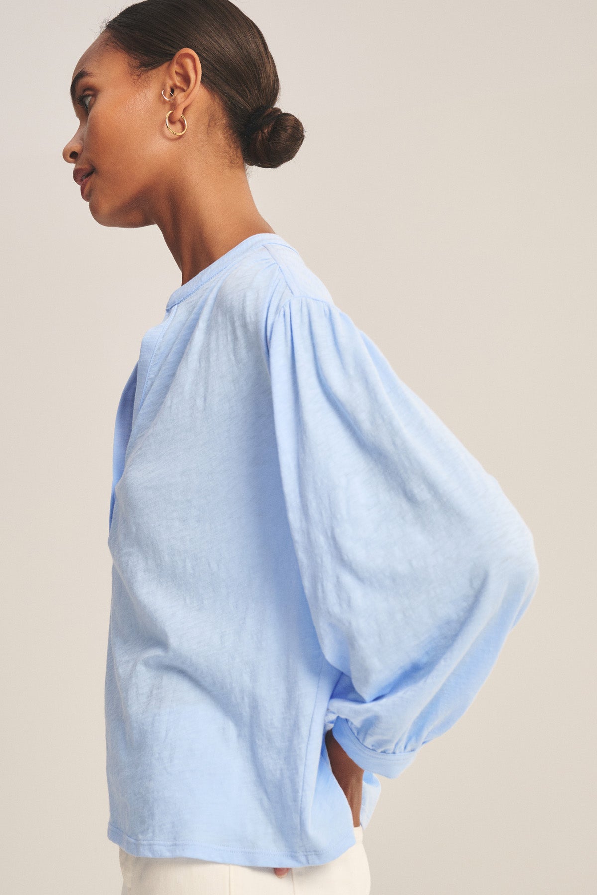 Woman in profile wears the KNOX TEE by Velvet by Graham & Spencer, a relaxed swing top with V-neckline and 3/4 sleeves, paired with white pants against a plain background.