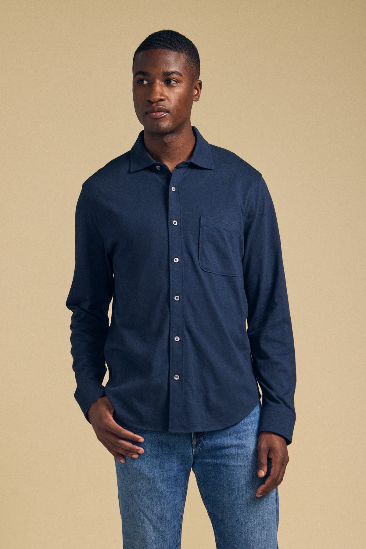 A man wearing the JONAH SHIRT by Velvet by Graham & Spencer and blue jeans stands against a plain beige background, looking slightly to the side.-41859678896321