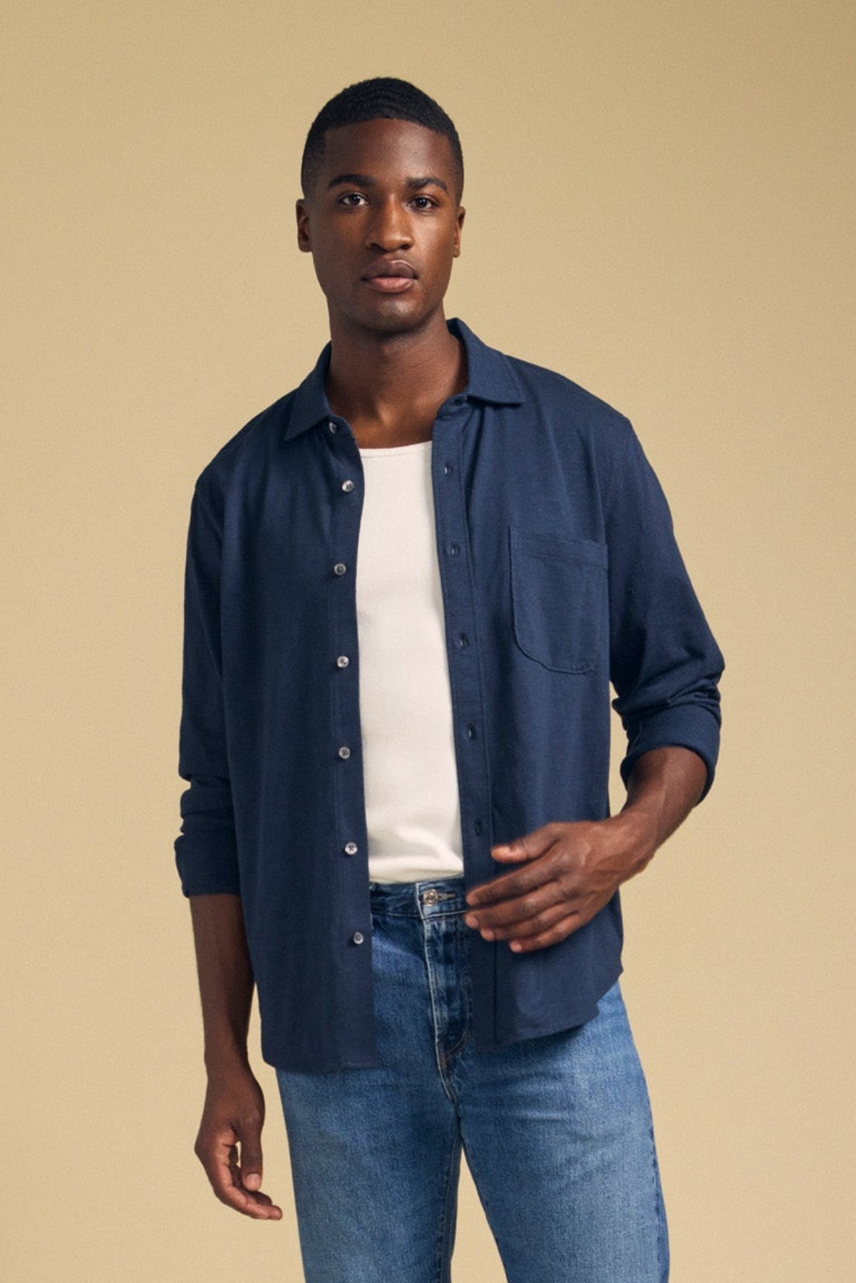 A person wearing the JONAH SHIRT by Velvet by Graham & Spencer, layered over a white t-shirt and paired with blue jeans, stands against a plain beige background.-41859679060161