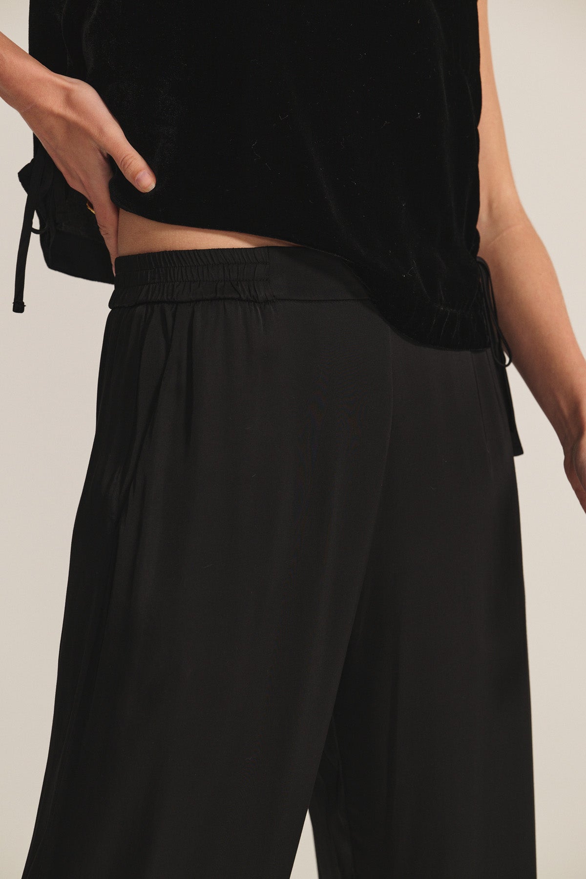   Model wearing the LARKIN PANT by Velvet by Graham & Spencer—black, loose-fitting wide-leg satin pants paired with a black top. Effortlessly flattering fit for everyday wear, shown from shoulders to knees against a neutral background. 