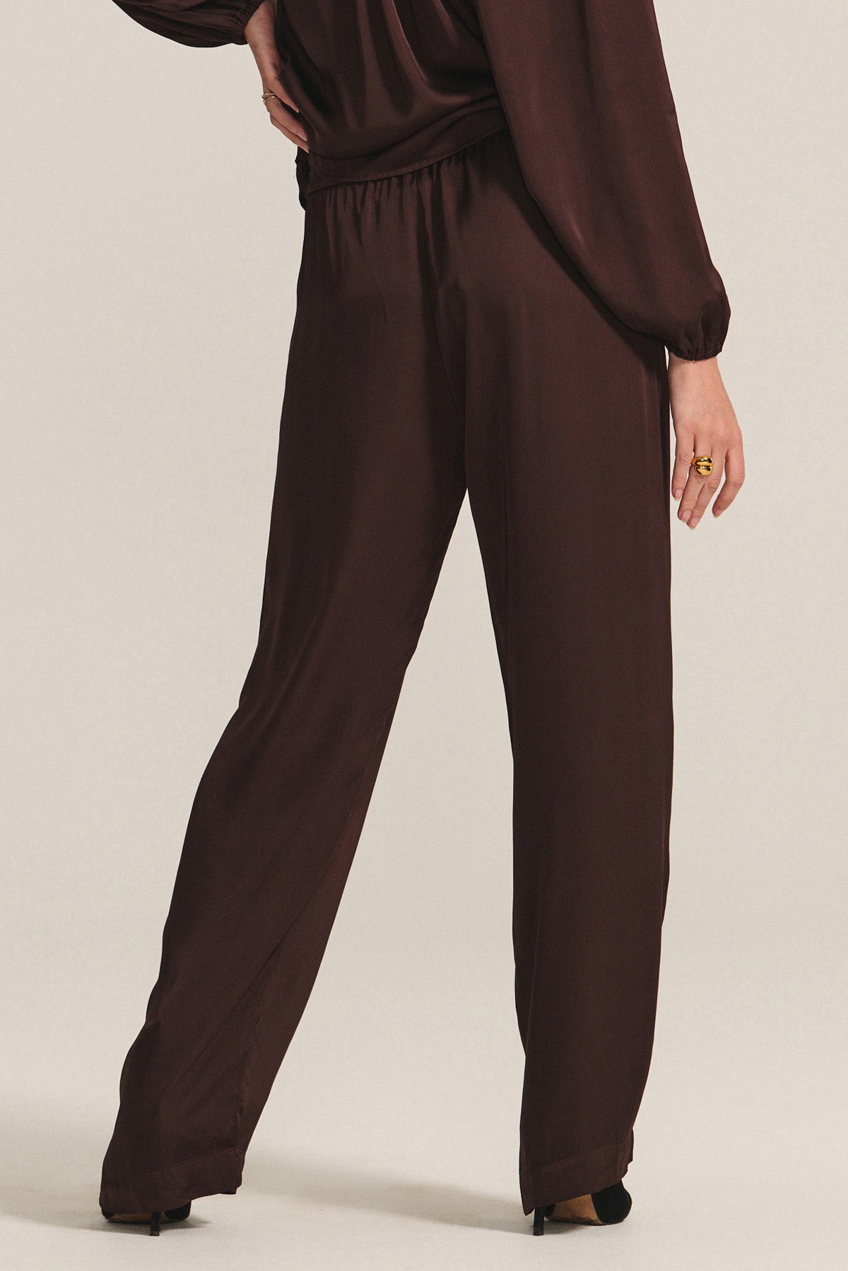   A person wears the LARKIN PANT by Velvet by Graham & Spencer—loose-fitting, dark brown wide-leg satin pants styled with a matching long-sleeve top for a flattering fit and stylish everyday wear. 