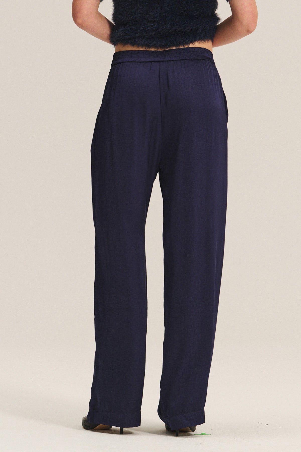 A person shown from the back wears Velvet by Graham & Spencer's LARKIN PANT in navy blue satin with a flattering wide-leg fit and a black sleeveless top against a light background—perfect for effortless everyday style.-40263652999361