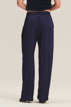 A person shown from the back wears Velvet by Graham & Spencer's LARKIN PANT in navy blue satin with a flattering wide-leg fit and a black sleeveless top against a light background—perfect for effortless everyday style.