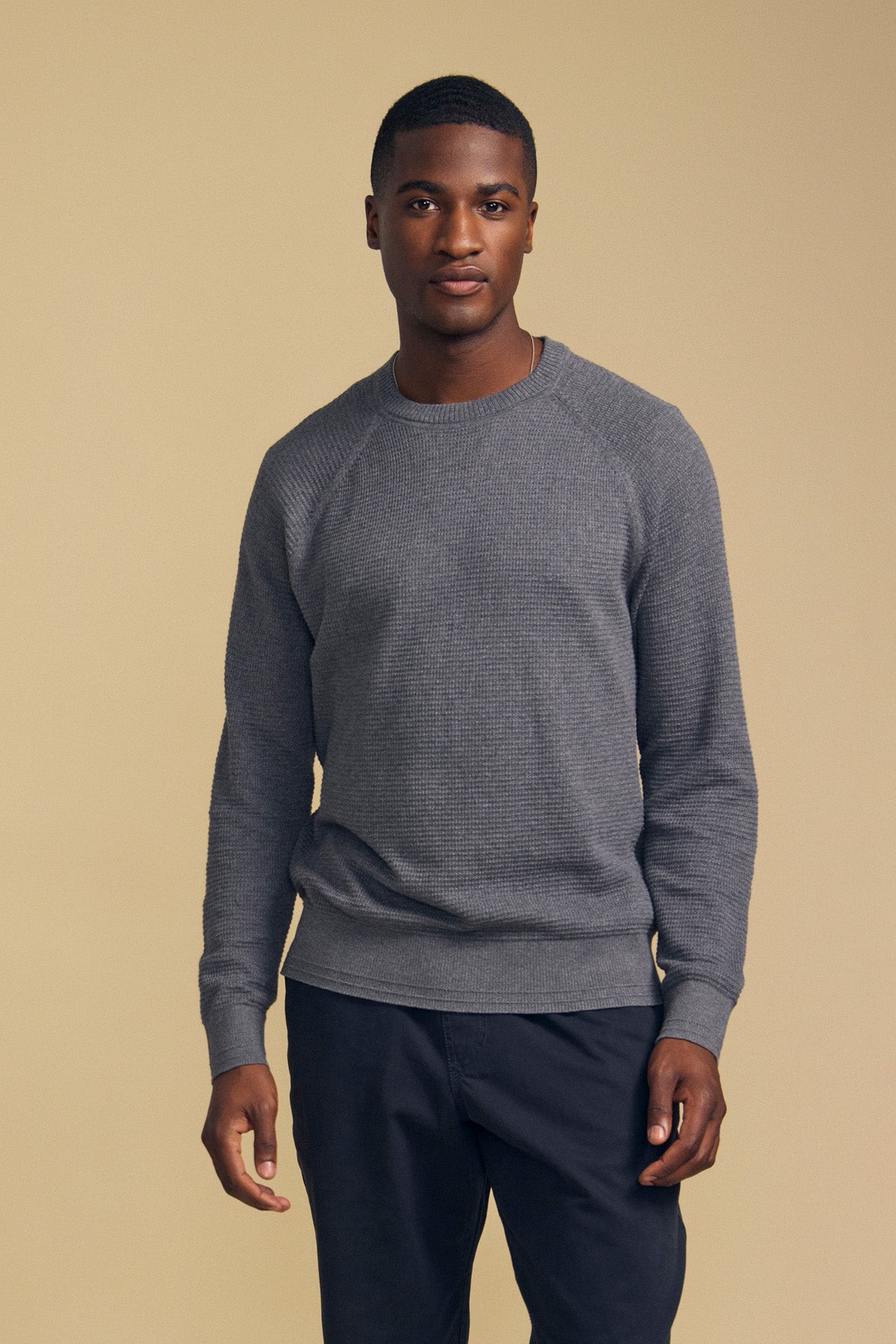 A man stands against a beige background, wearing the Velvet by Graham & Spencer AUGIE Cotton Cashmere Sweater with a textured gray crew neckline and dark pants, looking directly at the camera with a neutral expression.-42092443500737
