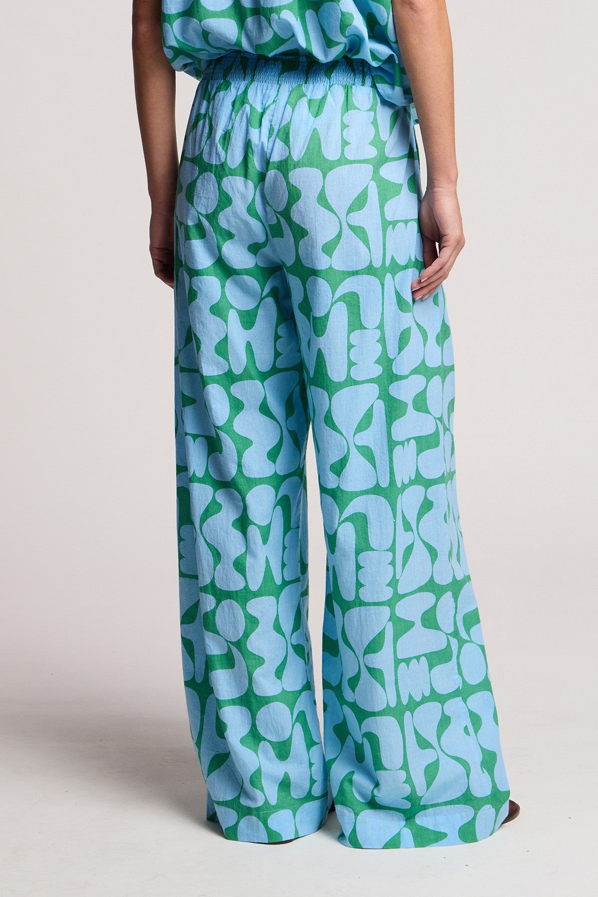 A person models the TRIXIE PANT by Velvet by Graham & Spencer, featuring wide-leg printed cotton cambric with blue and green abstract patterns, viewed from the back against a plain background.-41645194608833