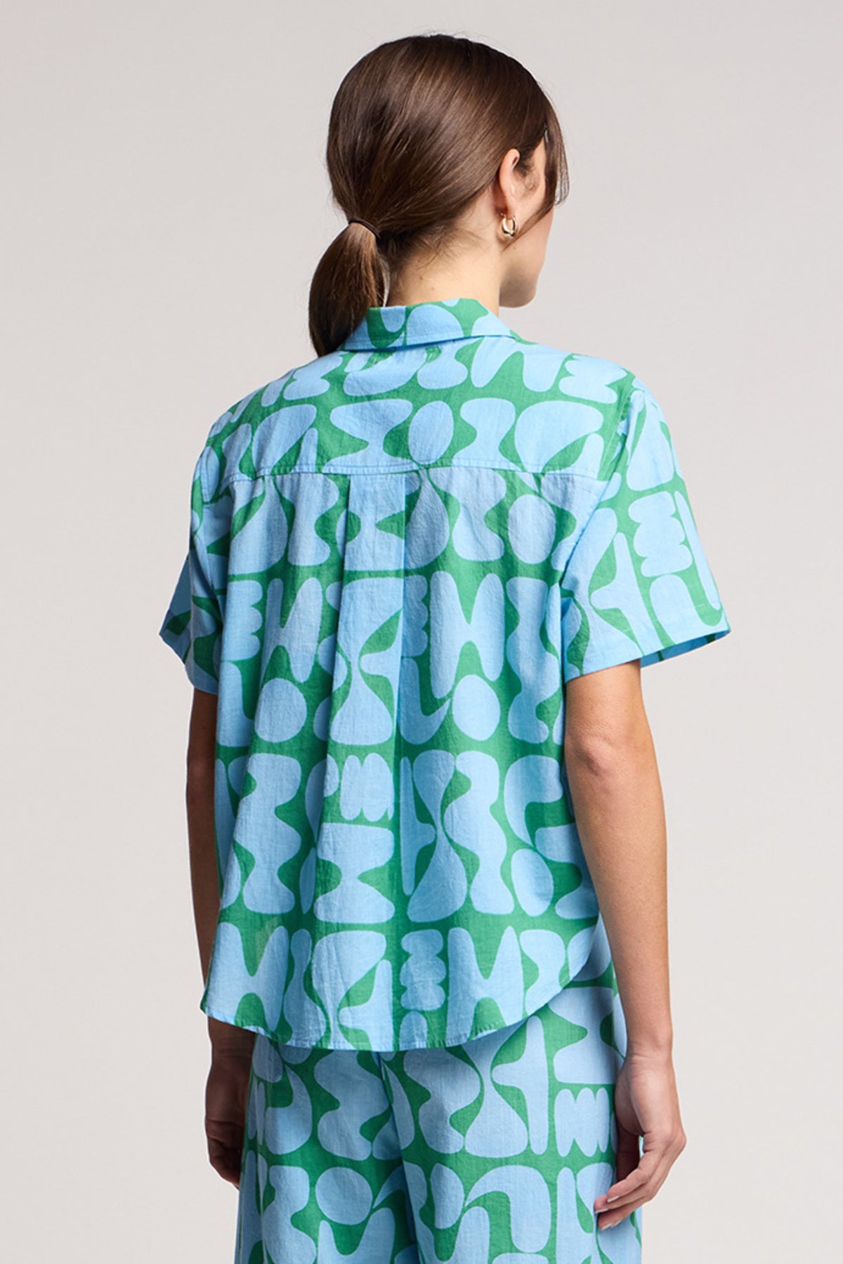 Person with back to camera wearing Velvet by Graham & Spencer’s MARINE SHIRT in light blue and green cotton cambric, featuring an abstract pattern, paired with matching pants.-41645083754689