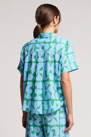 Person with back to camera wearing Velvet by Graham & Spencer’s MARINE SHIRT in light blue and green cotton cambric, featuring an abstract pattern, paired with matching pants.