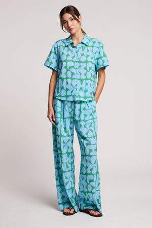 A woman wears the Velvet by Graham & Spencer MARINE SHIRT in light blue and green Lido print cotton cambric with matching wide-leg pants, standing against a plain background.