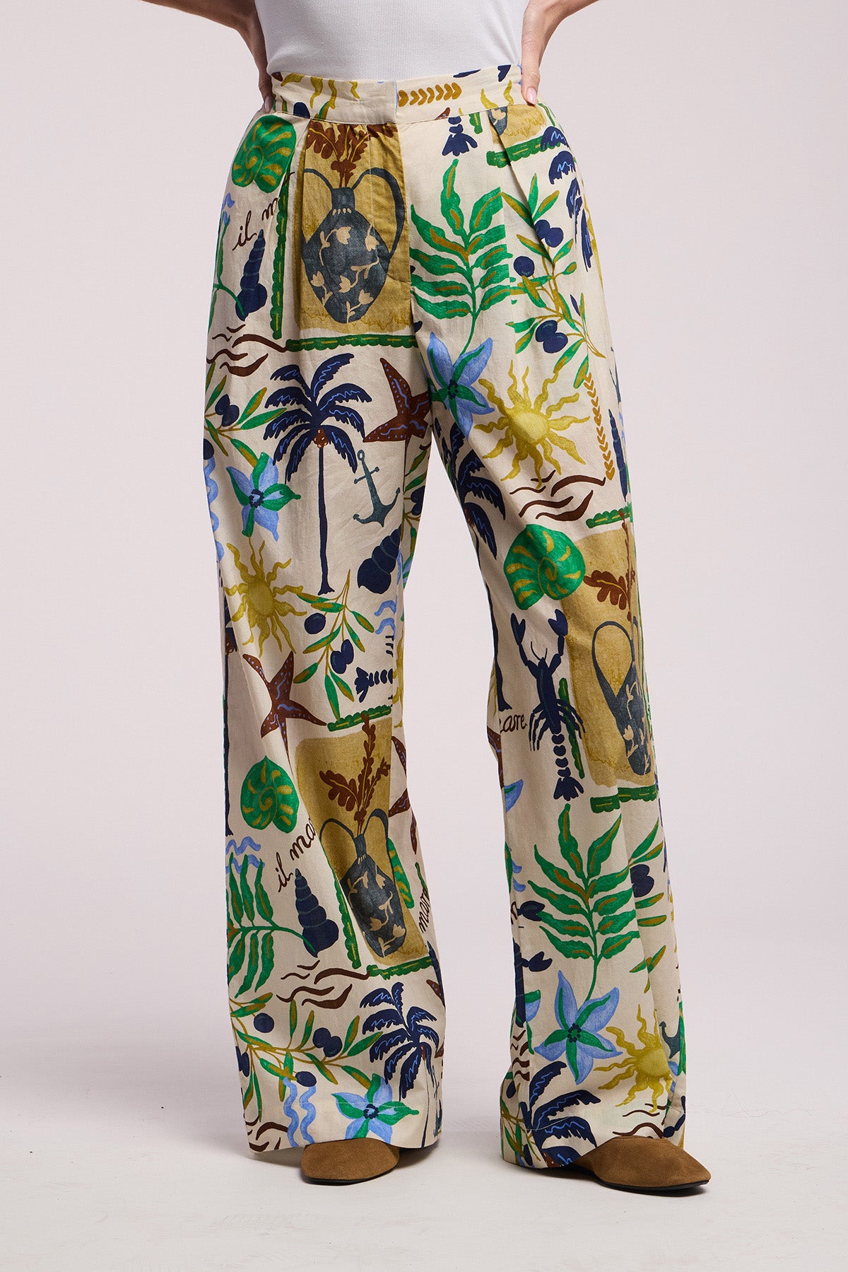 A person wears the TRIXIE PANT by Velvet by Graham & Spencer—cream-colored cotton cambric, wide leg silhouette with a colorful botanical print—paired with brown shoes against a plain background.