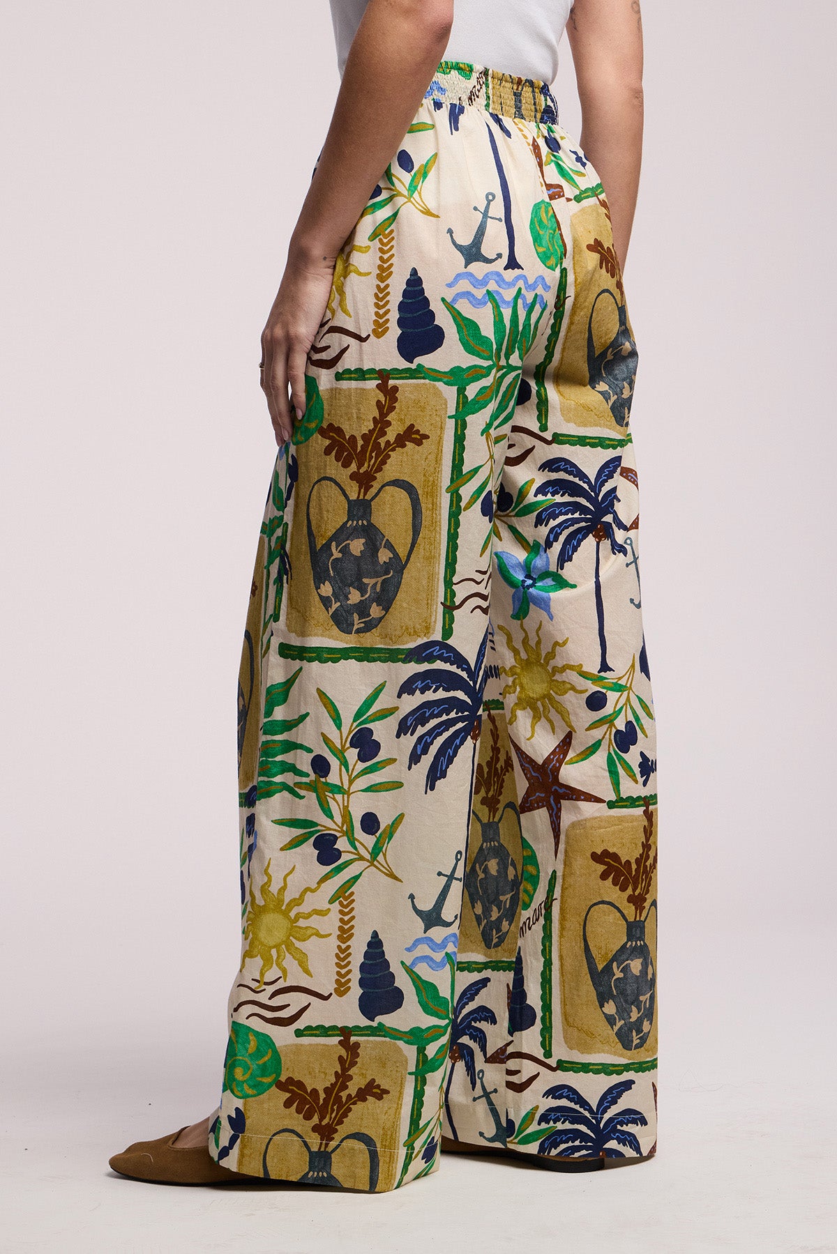 A person wears the TRIXIE PANT by Velvet by Graham & Spencer—cotton cambric statement pants featuring a colorful tropical print with plants, seashells, and anchors, and a wide leg silhouette against a plain background.-41527546118337
