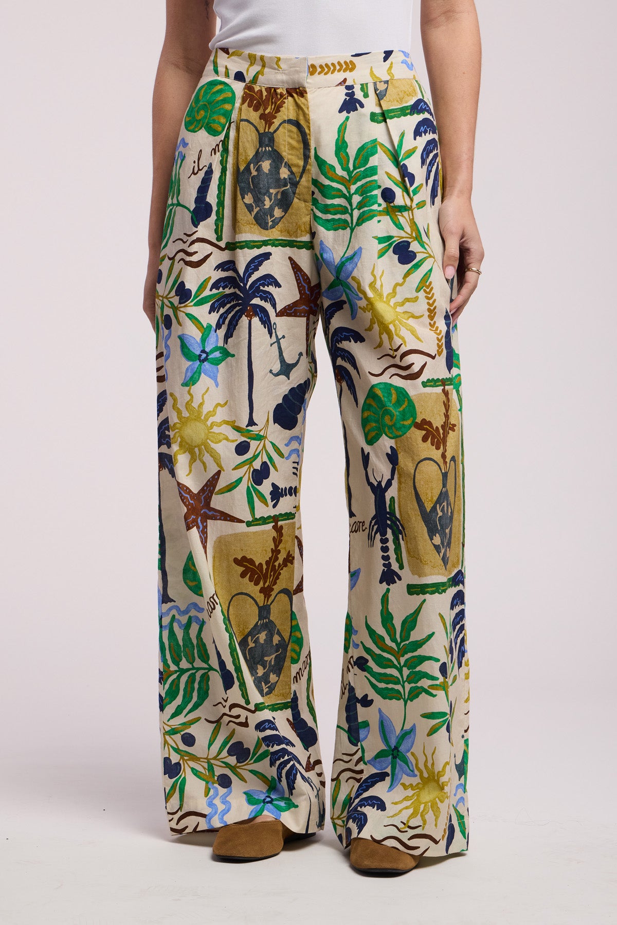 A person wears Velvet by Graham & Spencer’s TRIXIE PANT, a high-waisted, wide-leg cotton cambric pant with a colorful botanical and abstract print, standing against a plain background.