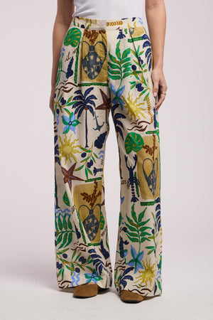 A person wears Velvet by Graham & Spencer’s TRIXIE PANT, a high-waisted, wide-leg cotton cambric pant with a colorful botanical and abstract print, standing against a plain background.