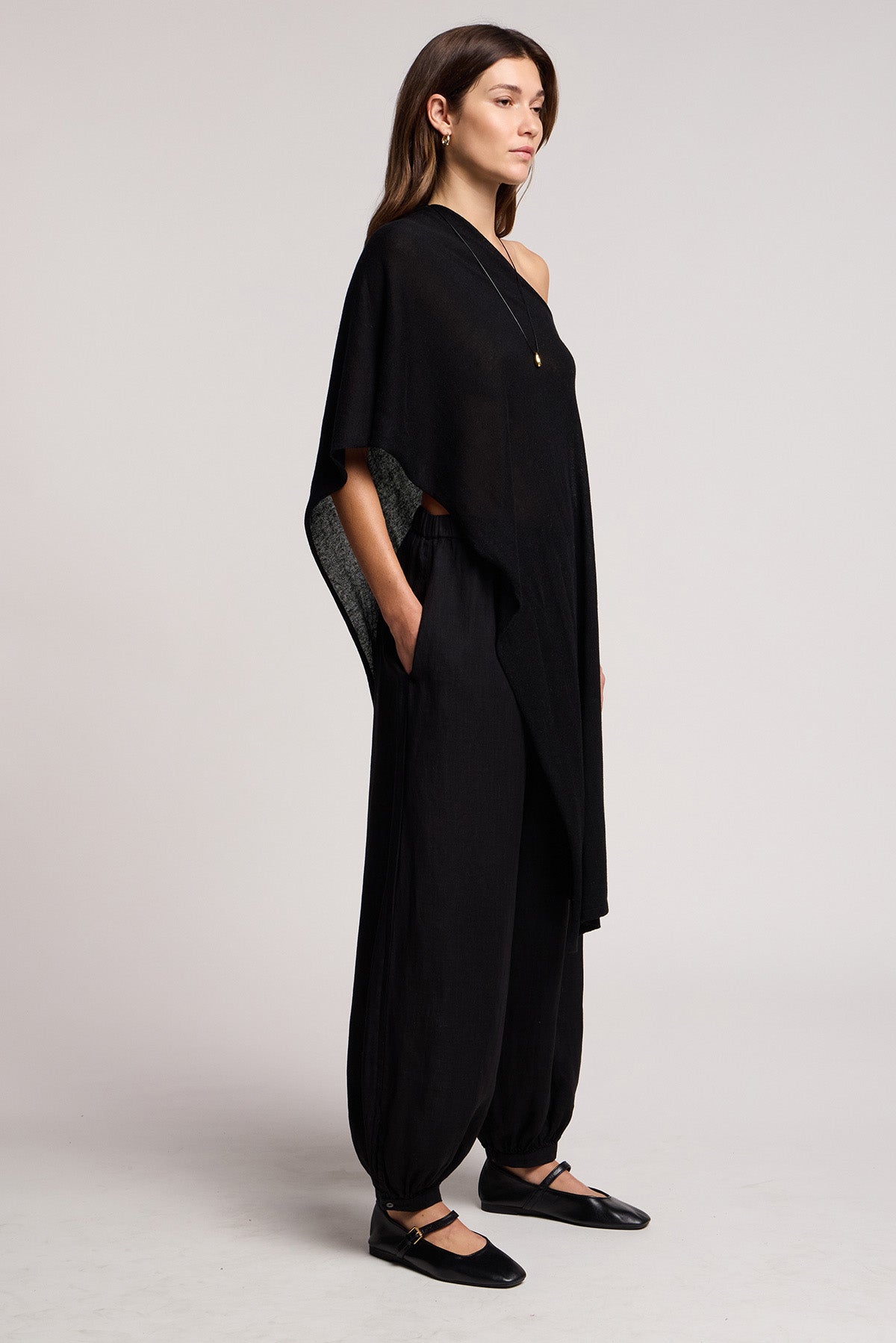 A woman stands in profile against a plain background wearing the Velvet by Graham & Spencer FLOREN SWEATER, paired with black wide-leg pants and black flats.