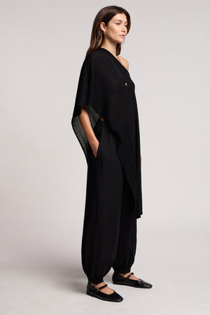 A woman stands in profile against a plain background wearing the Velvet by Graham & Spencer FLOREN SWEATER, paired with black wide-leg pants and black flats.