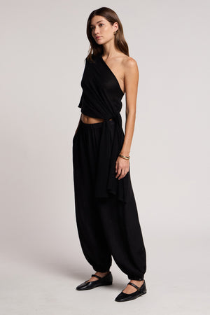 Woman stands in a studio wearing the Velvet by Graham & Spencer FLOREN SWEATER, paired with loose black pants and black flats, her hands in pockets and expression neutral.