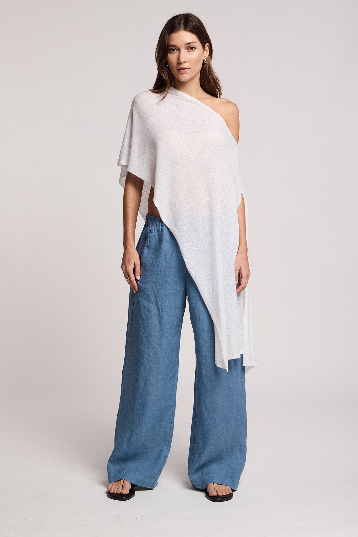 A woman stands against a neutral background wearing the FLOREN SWEATER by Velvet by Graham & Spencer, paired with loose blue pants and black sandals.