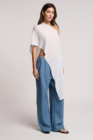 A woman stands in a studio wearing the FLOREN SWEATER by Velvet by Graham & Spencer, paired with loose blue pants and black sandals. She faces forward with a neutral expression.
