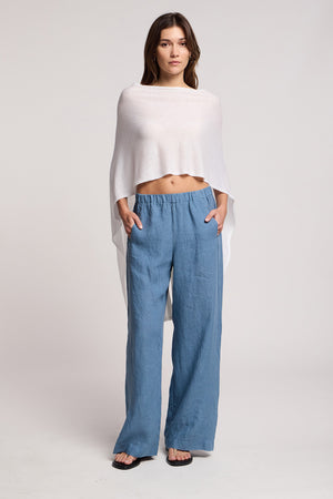 A woman faces forward against a plain background, wearing the FLOREN SWEATER by Velvet by Graham & Spencer, paired with blue wide-leg pants and black sandals.