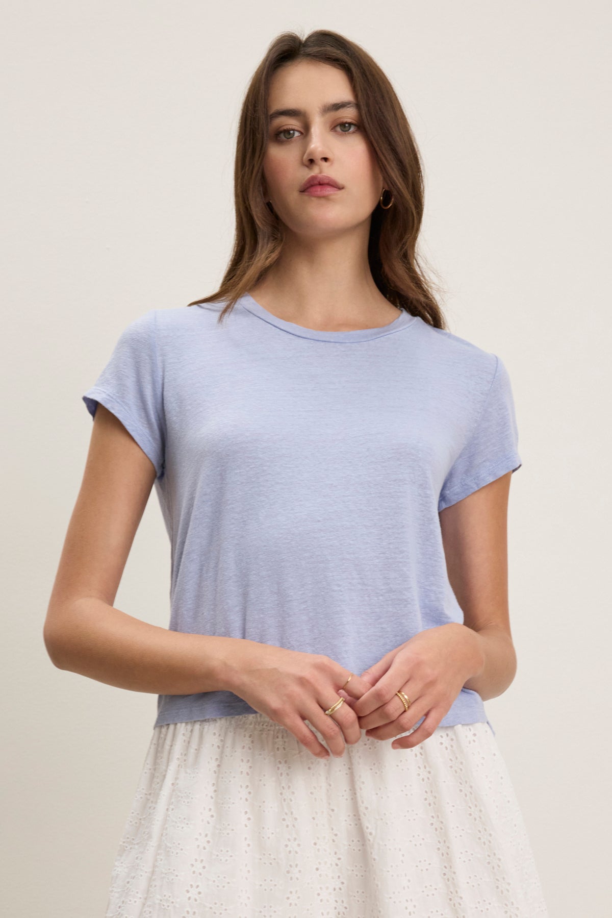   A woman wears the Velvet by Graham & Spencer CASEY LINEN KNIT TEE in light blue with a white skirt, standing against a plain light background. 