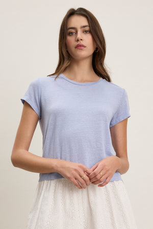 A woman wears the Velvet by Graham & Spencer CASEY LINEN KNIT TEE in light blue with a white skirt, standing against a plain light background.