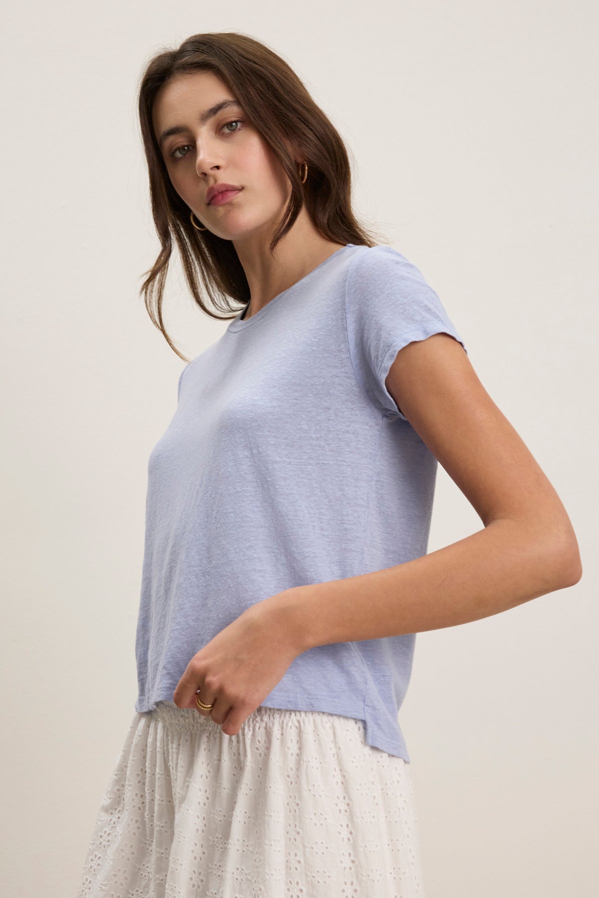 A woman wears the CASEY LINEN KNIT TEE by Velvet by Graham & Spencer in light blue with a white eyelet skirt, standing against a plain, light background.-39123274858689
