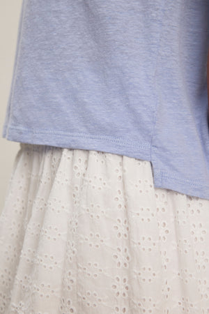 A close-up of the CASEY LINEN KNIT TEE in light blue from Velvet by Graham & Spencer, styled with a white, eyelet-patterned skirt.