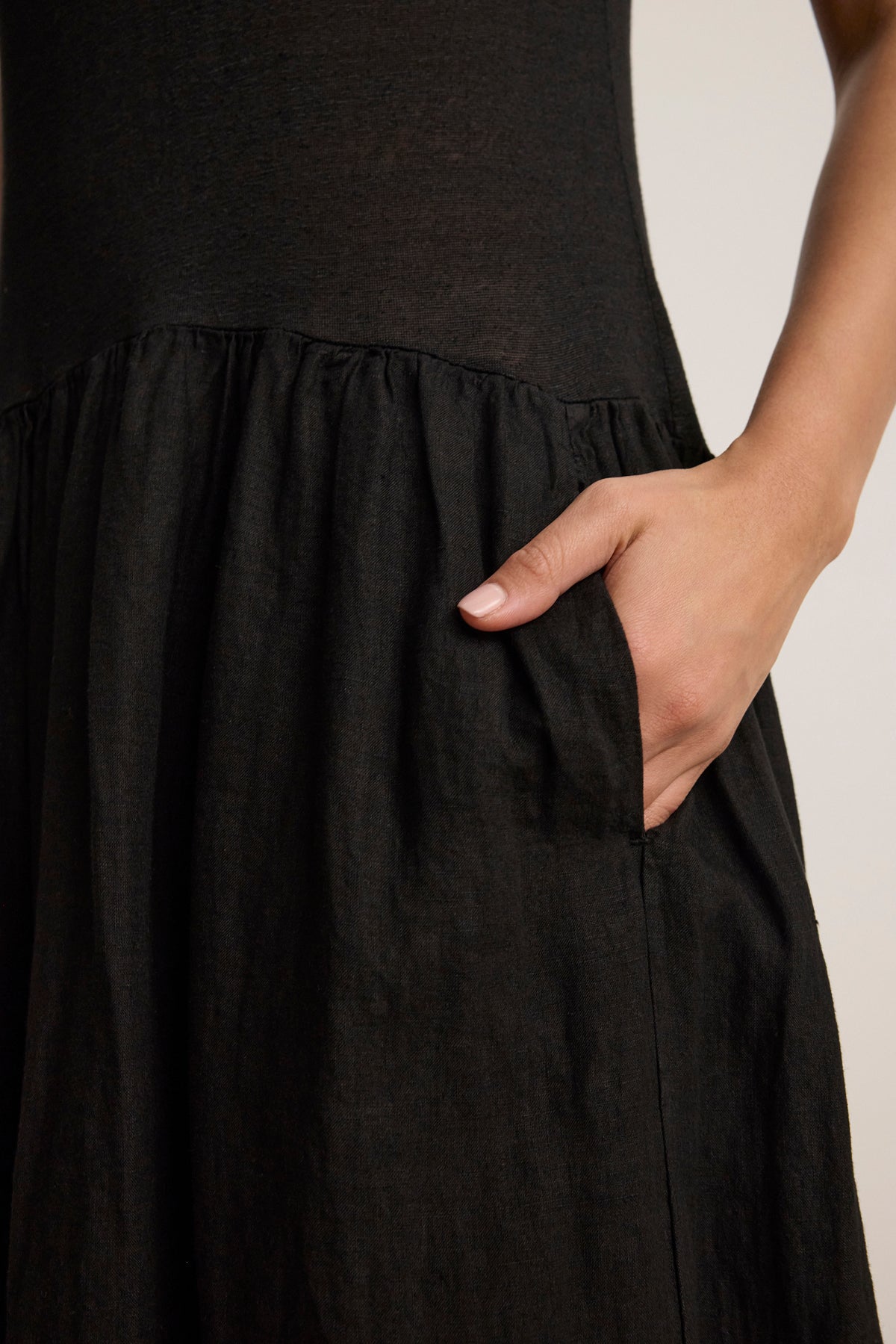 A person wearing the MABLE LINEN KNIT DRESS by Velvet by Graham & Spencer, a black midi-length linen blend dress with a gathered skirt, places their right hand in the side pocket.-Hover Image