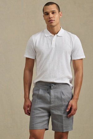A man wearing a white polo shirt and Velvet by Graham & Spencer's DAMIEN LINEN SHORT stands against a plain beige background.