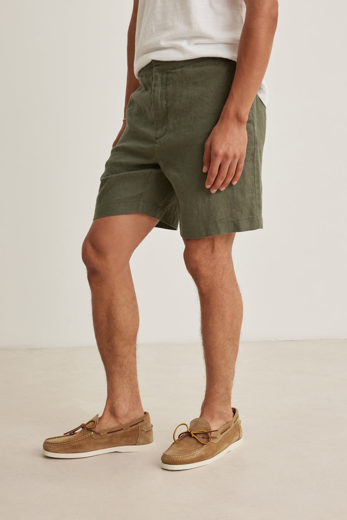 A person wears Velvet by Graham & Spencer's EAMON LINEN SHORT in olive green, paired with a white linen t-shirt and brown boat shoes, standing against a light background for an effortlessly versatile warm-weather look.-39152684630209