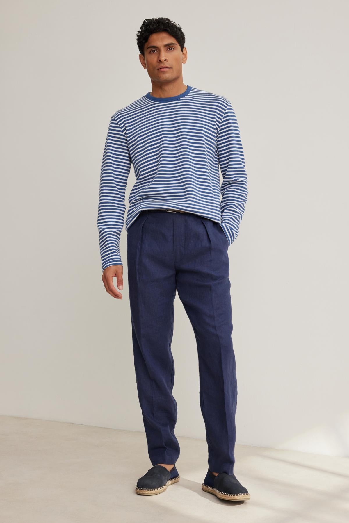   Man in a blue and white striped sweater, CANNON LINEN PANT by Velvet by Graham & Spencer, and black espadrilles stands against a plain background. 