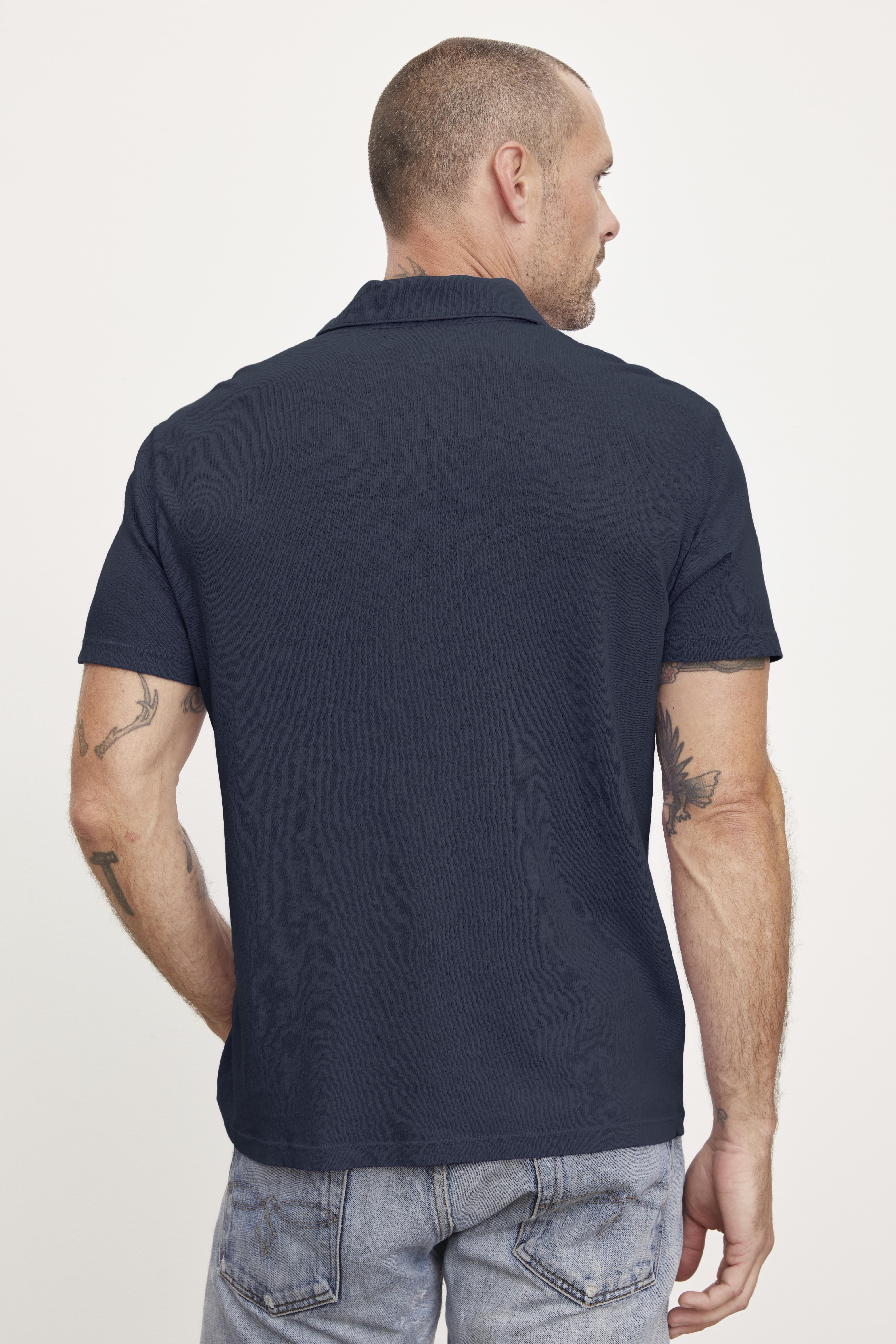   Man wearing a Velvet by Graham & Spencer BECK POLO and jeans, viewed from behind, with visible tattoos on his left arm. 