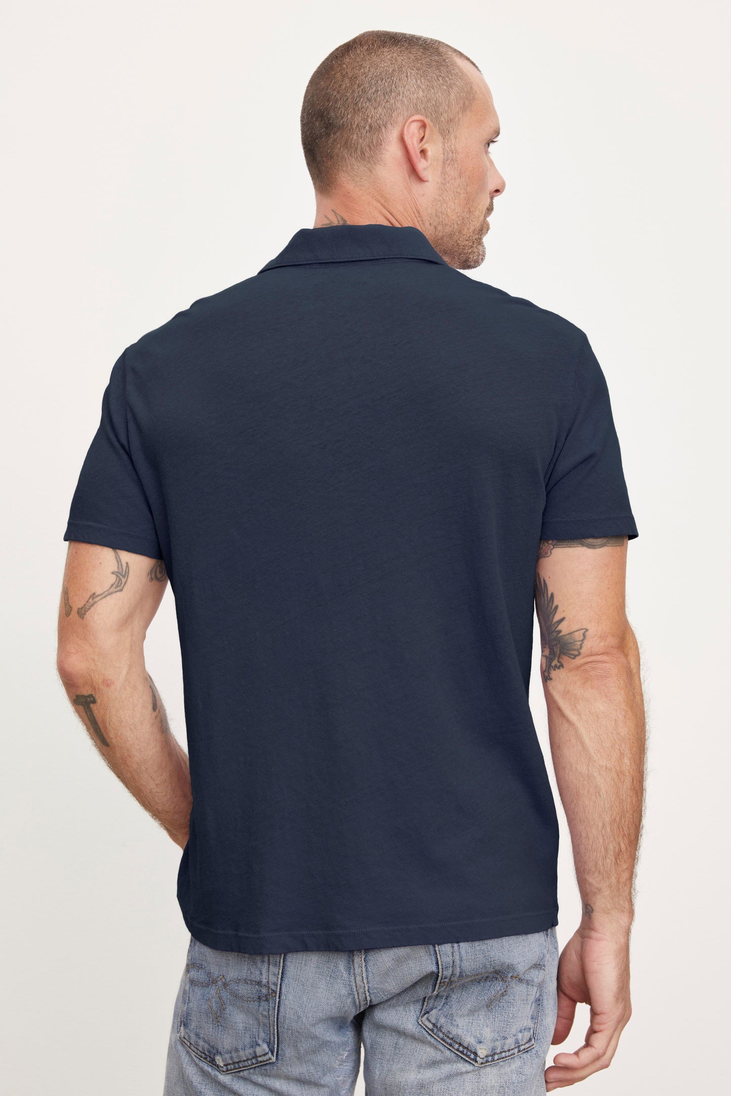 Man wearing a Velvet by Graham & Spencer BECK POLO and jeans, viewed from behind, with visible tattoos on his left arm.-36890691862721
