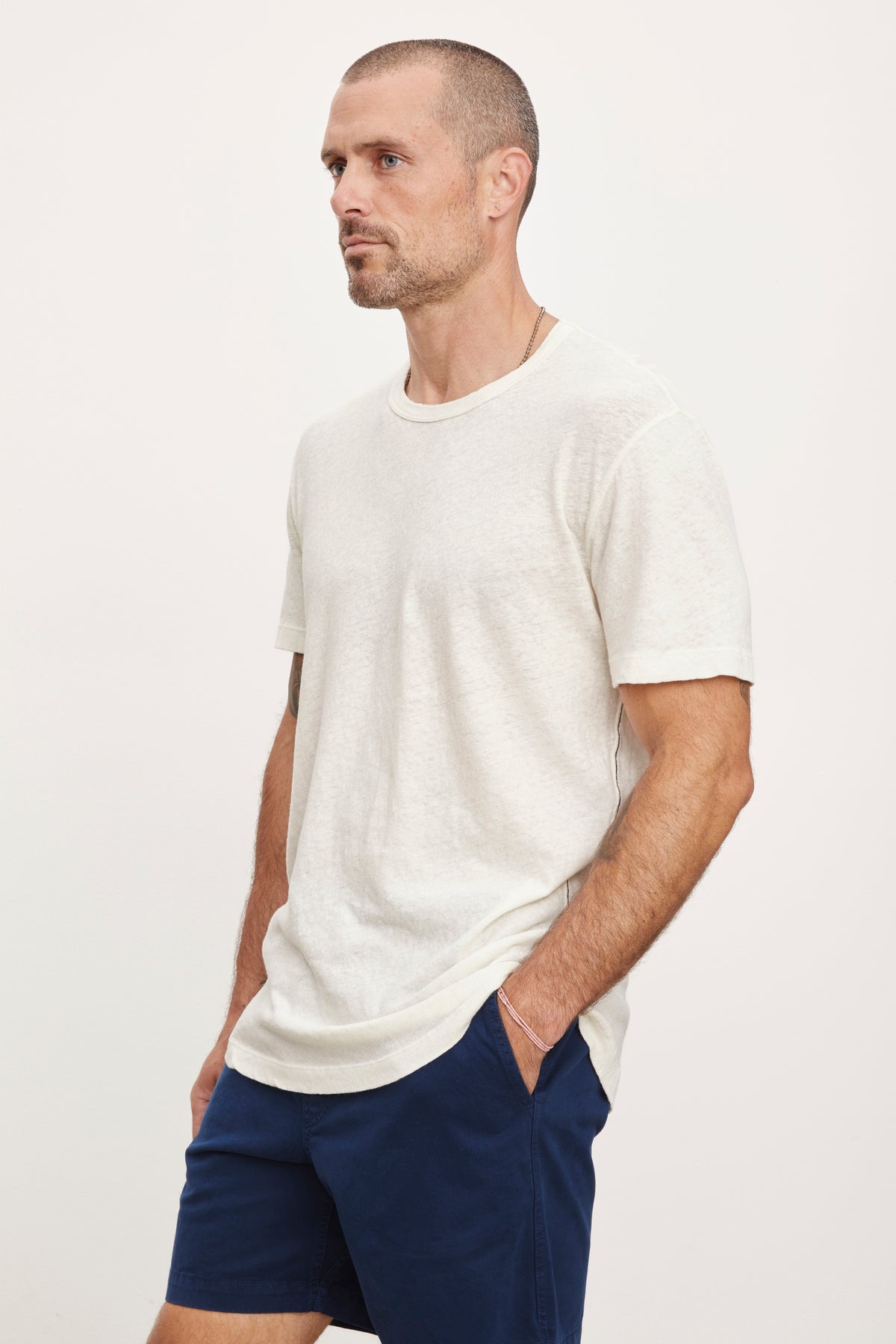 A man wearing a Velvet by Graham & Spencer Davey Tee and navy blue shorts, standing in profile against a white background.-36732521283777