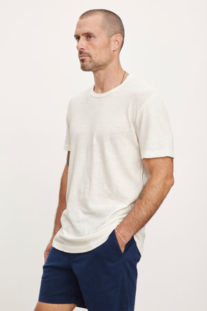 A man wearing a Velvet by Graham & Spencer Davey Tee and navy blue shorts, standing in profile against a white background.