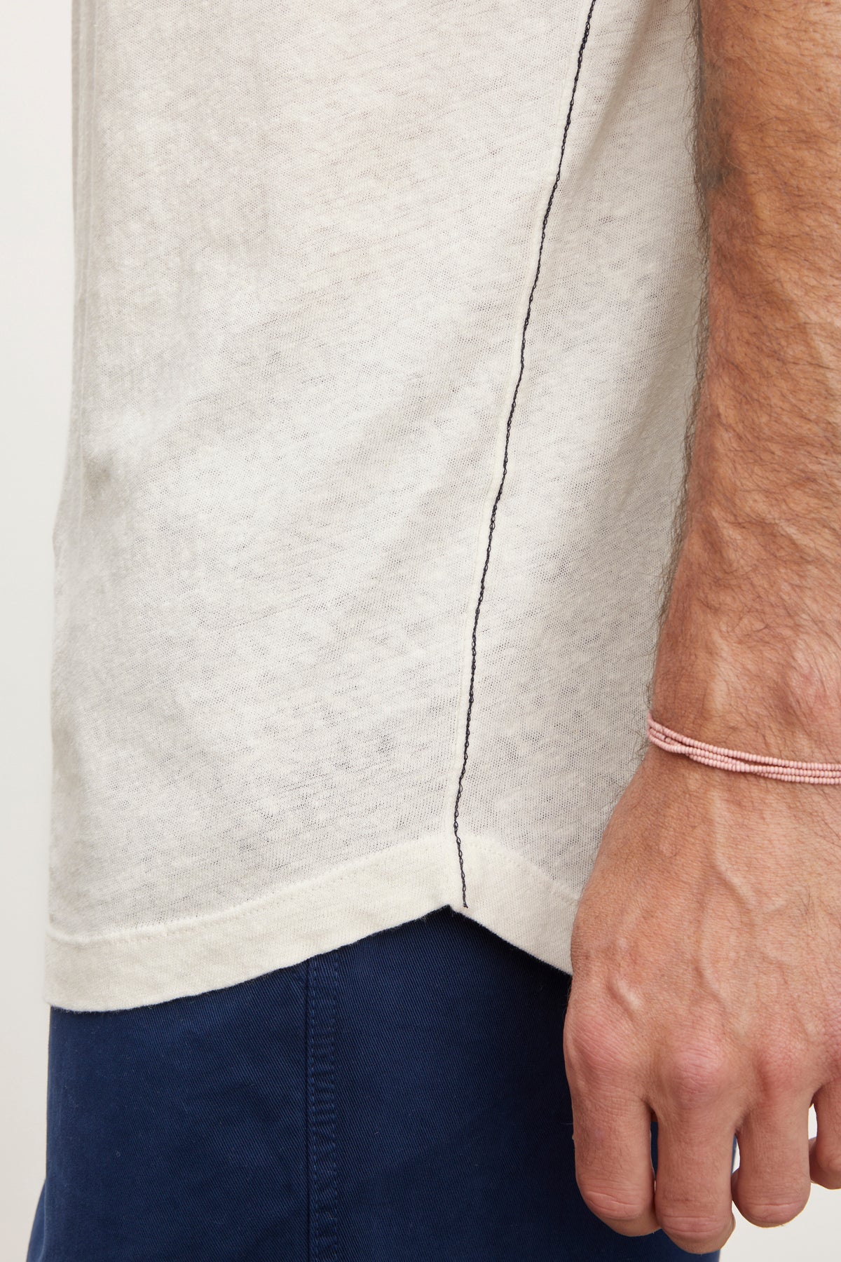 Close-up of a man's side, showing a Velvet by Graham & Spencer DAVEY TEE and navy pants, with a focus on the seam and his hand wearing a pink bracelet.-36732521349313