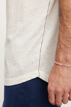 Close-up of a man's side, showing a Velvet by Graham & Spencer DAVEY TEE and navy pants, with a focus on the seam and his hand wearing a pink bracelet.