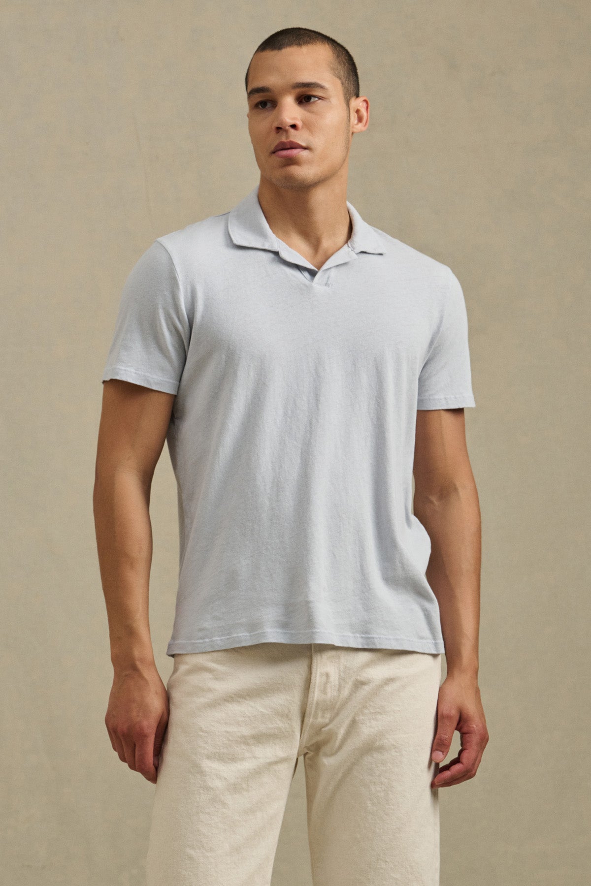 A man stands against a plain background, wearing the relaxed fit ASHTON POLO by Velvet by Graham & Spencer in light gray and off-white pants, looking slightly to the side.-41479914455233