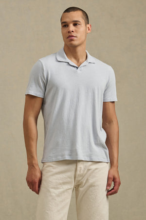 A man stands against a plain background, wearing the relaxed fit ASHTON POLO by Velvet by Graham & Spencer in light gray and off-white pants, looking slightly to the side.