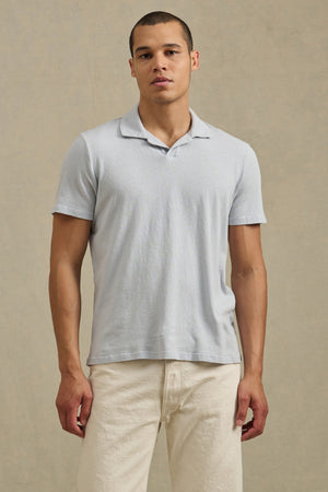 A man stands facing forward in the ASHTON POLO by Velvet by Graham & Spencer, a lightweight, relaxed fit cotton-linen blend shirt, paired with off-white pants against a neutral background.