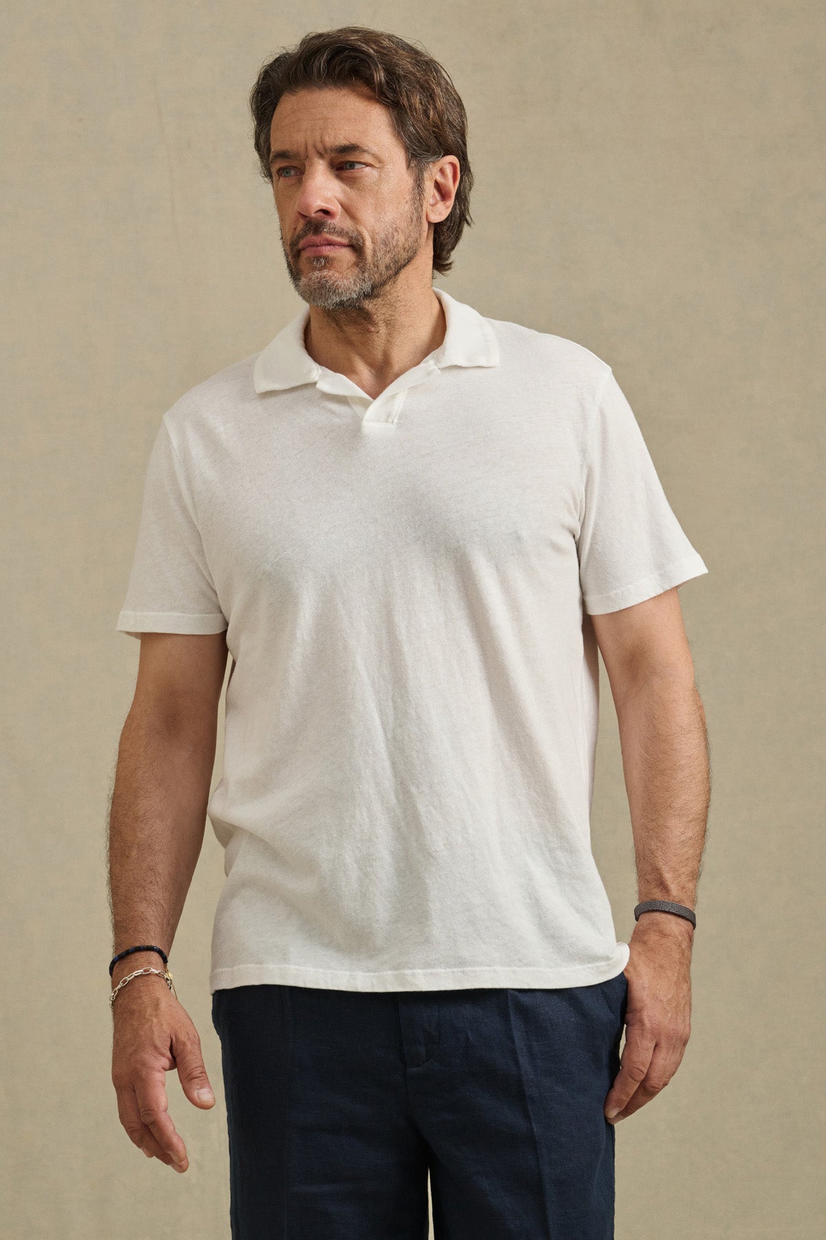 A bearded man wears the Velvet by Graham & Spencer ASHTON POLO in white, styled with dark pants, standing against a plain light background.