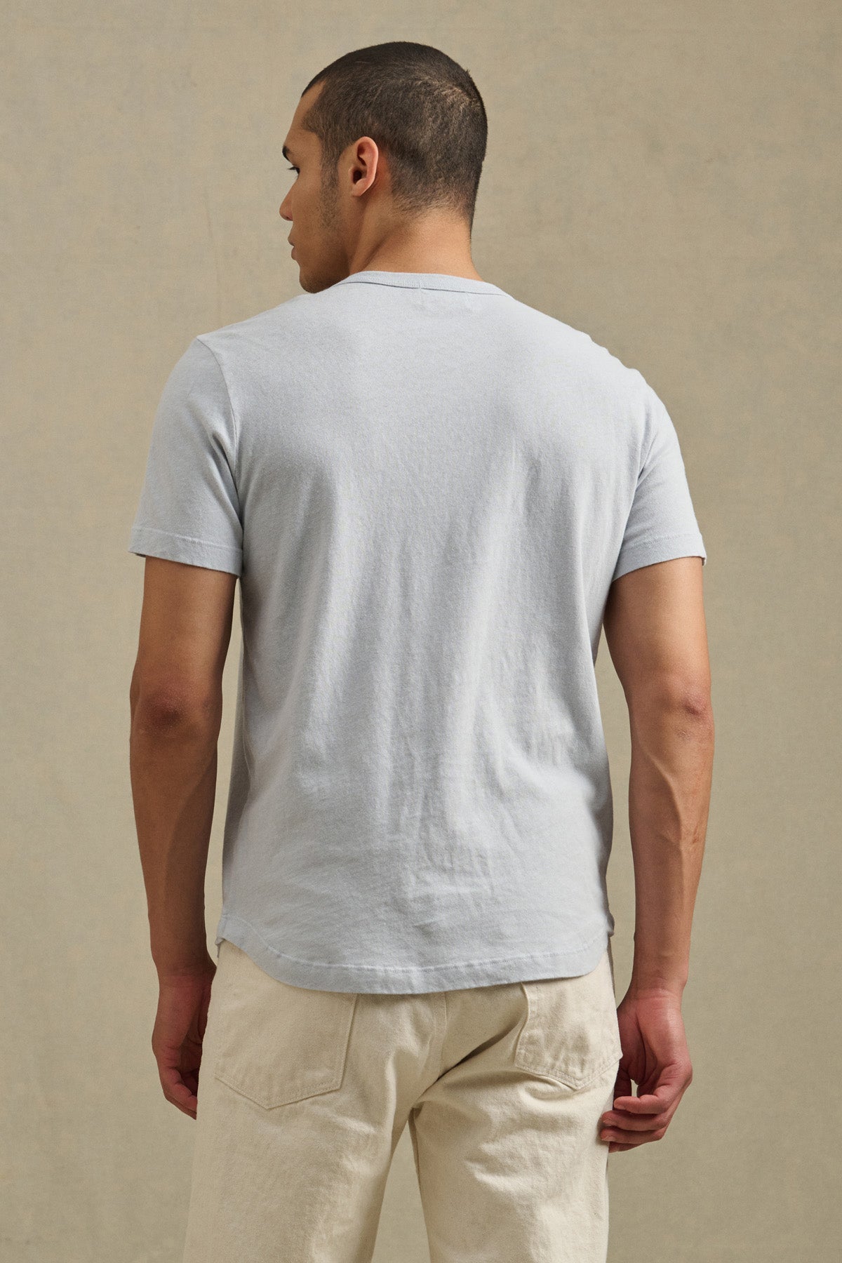A man faces away from the camera, wearing the LUKA TEE by Velvet by Graham & Spencer—a lightweight cotton-linen short sleeve crew neck t-shirt—paired with off-white pants against a neutral background.-41479919337665