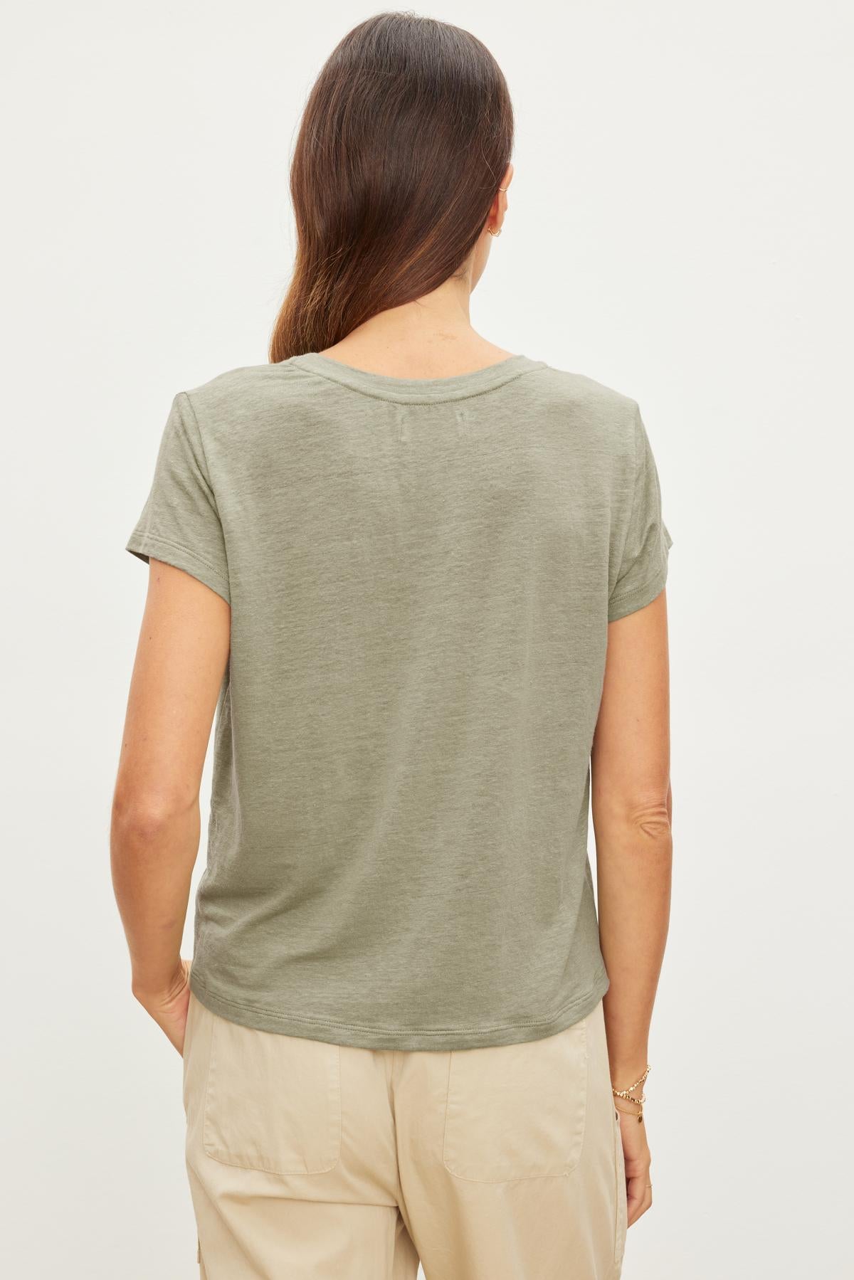 Rear view of a woman wearing a Velvet by Graham & Spencer CASEY LINEN KNIT CREW NECK TEE in green and beige pants, standing against a white background.-36909994115265