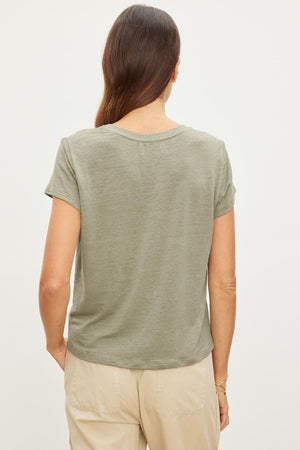 Rear view of a woman wearing a Velvet by Graham & Spencer CASEY LINEN KNIT CREW NECK TEE in green and beige pants, standing against a white background.