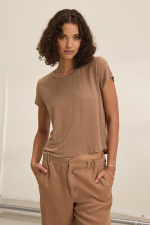 A person with curly hair wears the CASEY LINEN KNIT TEE by Velvet by Graham & Spencer and matching pants, both providing a flawless fit, standing with hands in pockets against a neutral background.