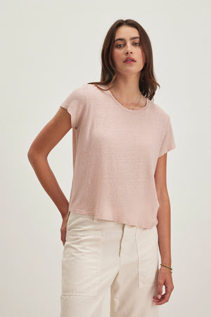 A person wearing a Velvet by Graham & Spencer CASEY LINEN KNIT TEE in light pink and off-white pants stands against a plain background.
