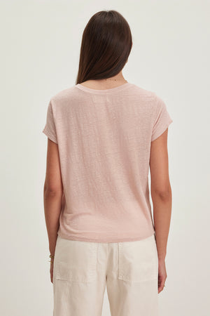 Person with long brown hair wears the CASEY LINEN KNIT TEE by Velvet by Graham & Spencer in light pink with a high-low hemline, paired with white pants, shown from the back against a plain background.