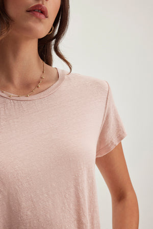 A woman in a CASEY LINEN KNIT TEE by Velvet by Graham & Spencer, styled in light pink with a flawless fit, paired with a necklace of small spheres, set against a light background.