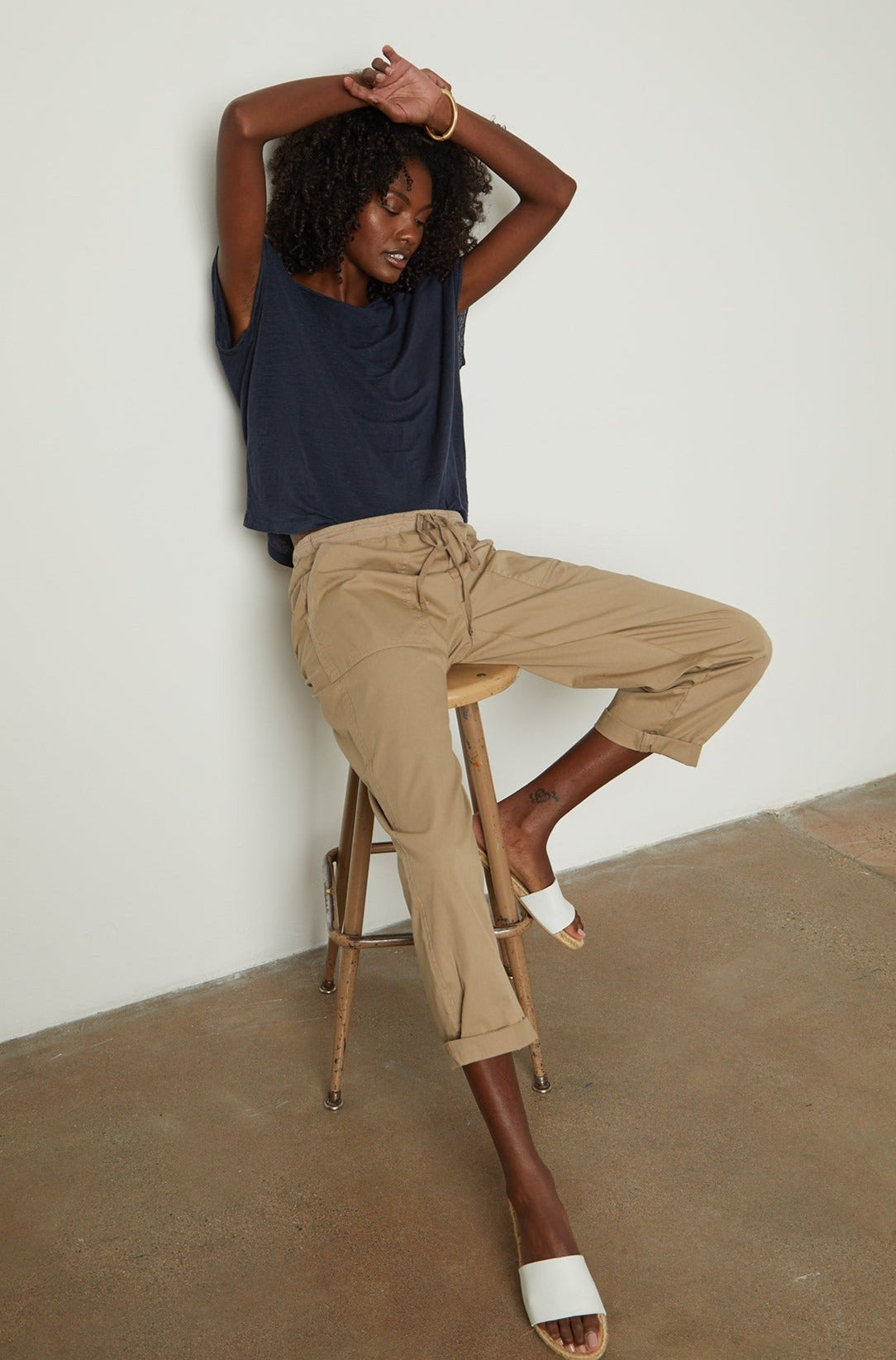 Model sitting on wooden stool in studio wearing Misty Pant in oak twill with Hudson Tee in baltic tucked-26496414941377