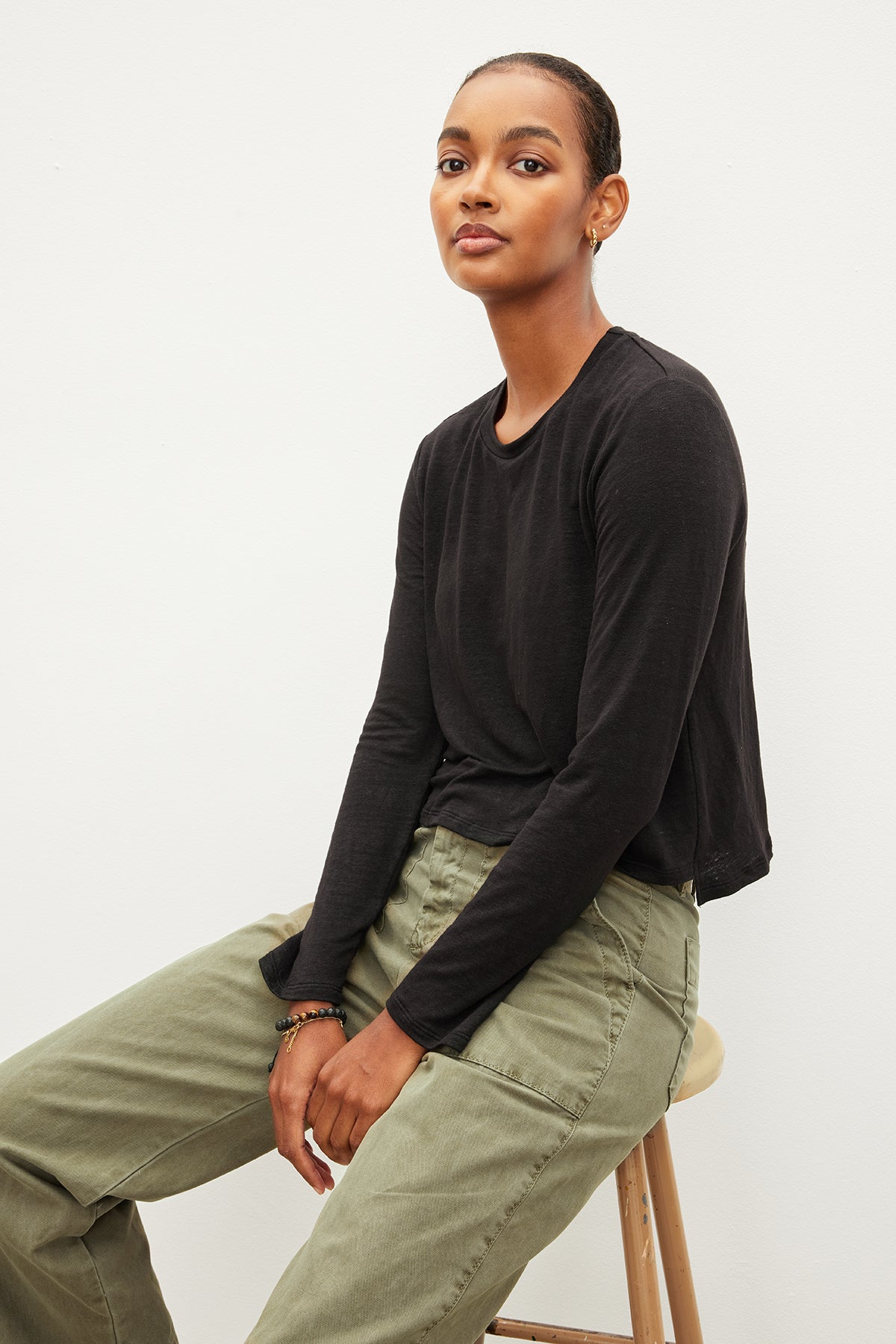 The model is wearing a slimmer fit Velvet by Graham & Spencer black long sleeve Kara Crew Neck Tee and lightweight olive green pants.-35967659475137