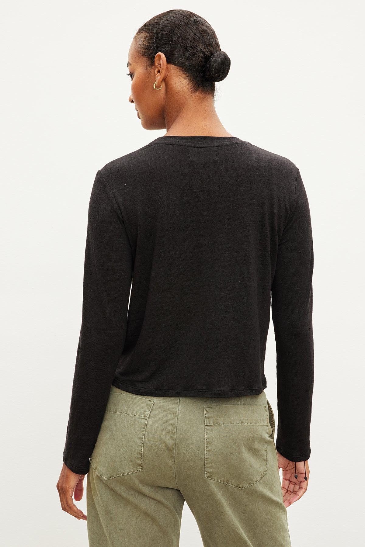   The back view of a woman wearing a lightweight linen Velvet by Graham & Spencer black long-sleeved KARA CREW NECK TEE and slimmer fit green pants. 